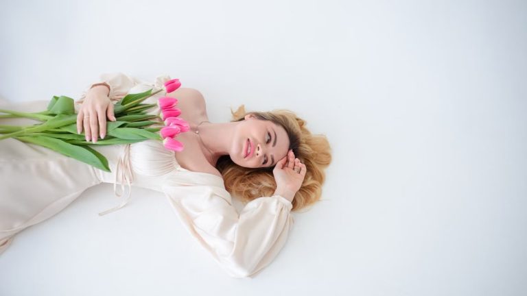 Relaxed woman lying with a bouquet of pink tulips on a minimalist white background. Spring vibes.